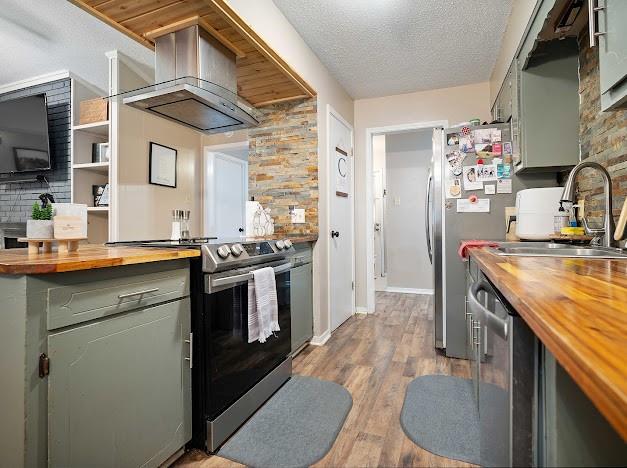 kitchen featuring a textured ceiling, sink, butcher block countertops, ventilation hood, and appliances with stainless steel finishes