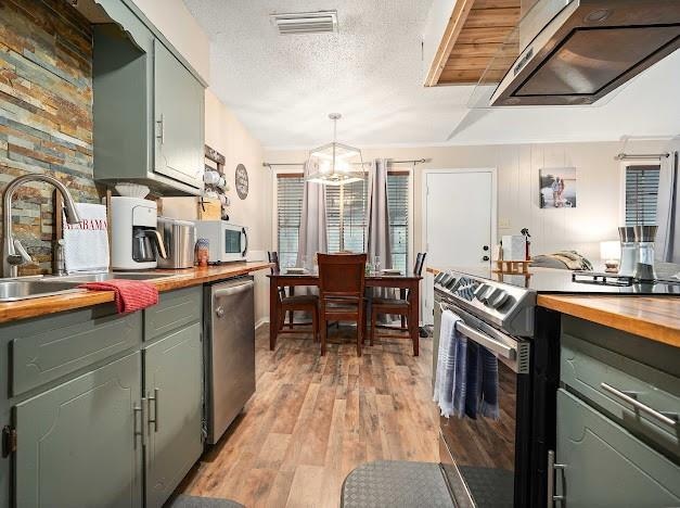 kitchen featuring light hardwood / wood-style floors, butcher block counters, hanging light fixtures, sink, and appliances with stainless steel finishes