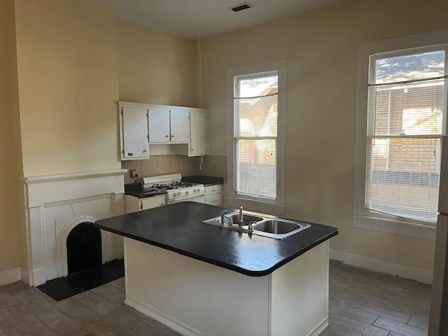 kitchen with plenty of natural light, a sink, white cabinets, white gas range oven, and dark countertops