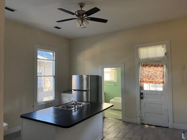 kitchen featuring visible vents, light wood-style flooring, freestanding refrigerator, a sink, and dark countertops