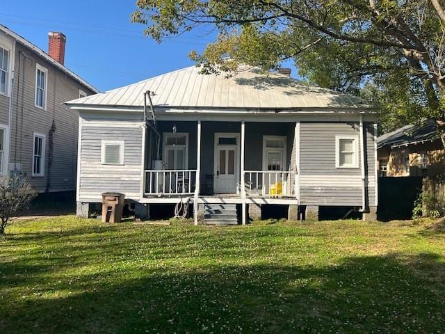 back of house with covered porch, a lawn, and metal roof