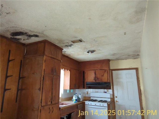 kitchen with white gas stove, a textured ceiling, and backsplash