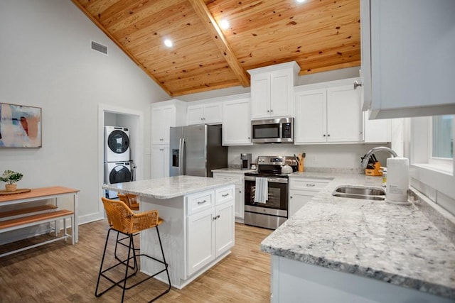 kitchen featuring white cabinets, a center island, wood ceiling, stainless steel appliances, and stacked washer and dryer