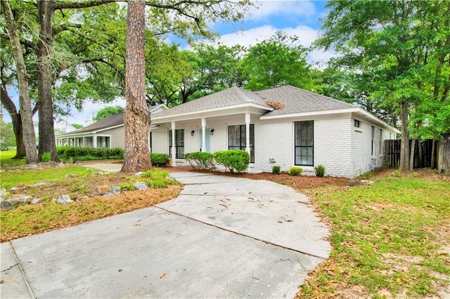single story home featuring covered porch, brick siding, fence, and roof with shingles