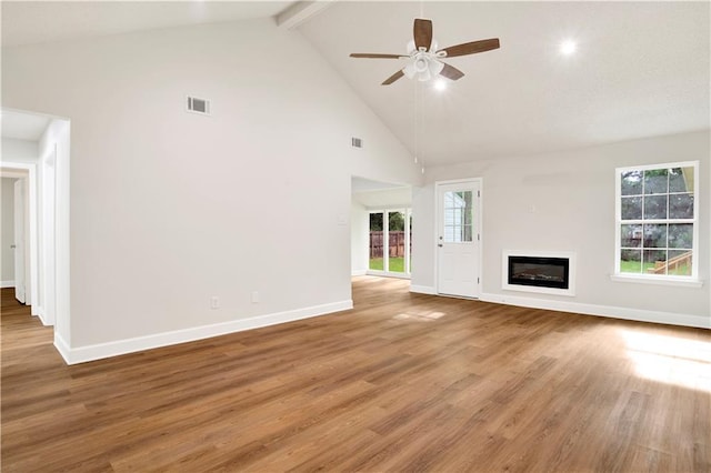 unfurnished living room featuring high vaulted ceiling, ceiling fan, baseboards, wood finished floors, and beam ceiling