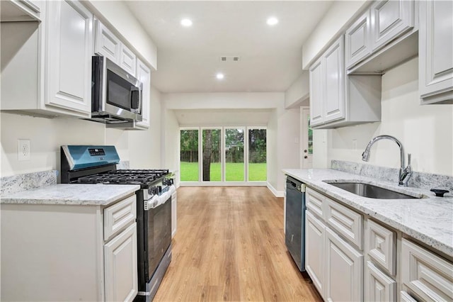 kitchen featuring stainless steel appliances, a sink, light wood-type flooring, recessed lighting, and white cabinetry