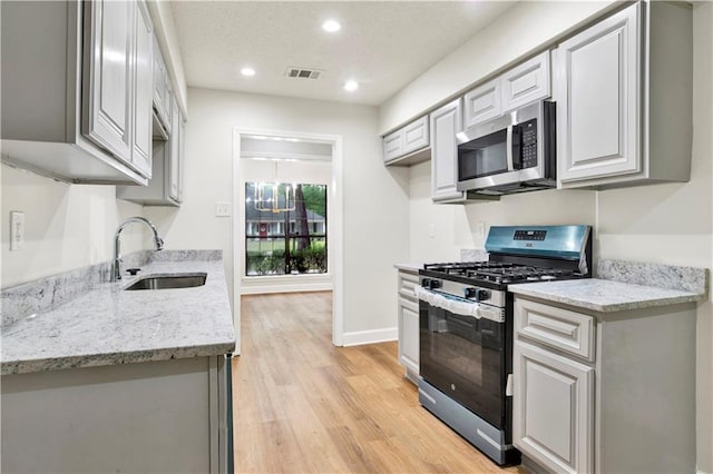 kitchen featuring appliances with stainless steel finishes, a sink, light wood-type flooring, recessed lighting, and light stone counters