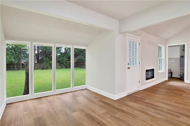 unfurnished living room featuring lofted ceiling, baseboards, light wood-type flooring, and a glass covered fireplace