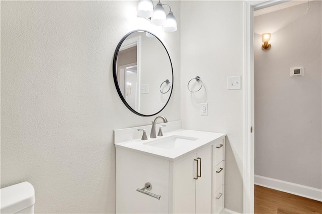 half bathroom featuring vanity, toilet, wood finished floors, and baseboards