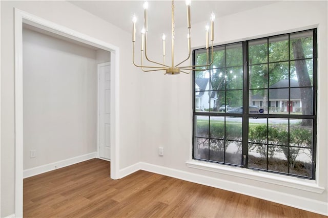 unfurnished dining area with a chandelier, wood finished floors, and baseboards