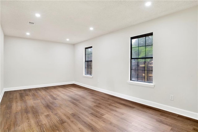 unfurnished room with plenty of natural light, wood finished floors, recessed lighting, and baseboards