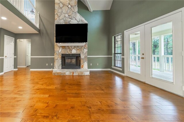 unfurnished living room with a fireplace, high vaulted ceiling, wood-type flooring, and french doors