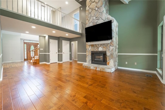 unfurnished living room with a stone fireplace, a towering ceiling, and hardwood / wood-style flooring