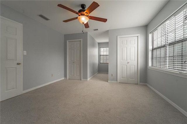 unfurnished bedroom featuring light carpet, ceiling fan, and multiple closets