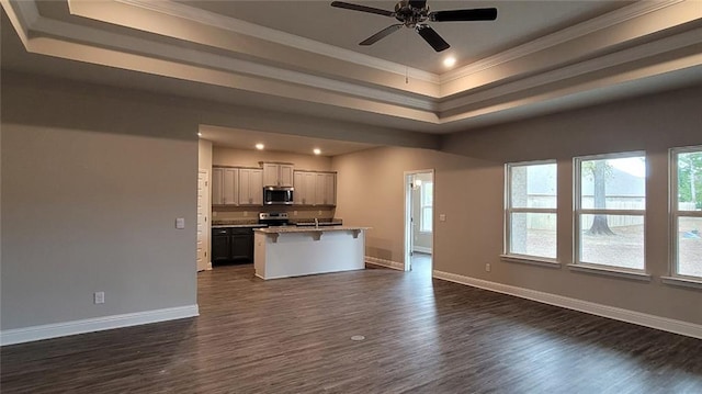 kitchen featuring a breakfast bar area, appliances with stainless steel finishes, dark hardwood / wood-style floors, a center island with sink, and a raised ceiling