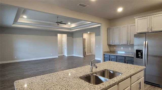 kitchen featuring sink, ceiling fan, stainless steel refrigerator with ice dispenser, a tray ceiling, and light stone countertops