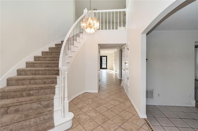 foyer entrance featuring visible vents, ornamental molding, a chandelier, tile patterned flooring, and stairs