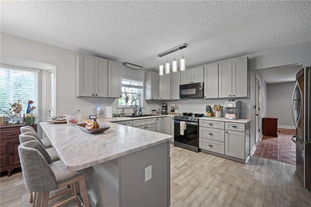 kitchen with pendant lighting, gray cabinetry, kitchen peninsula, and stainless steel appliances