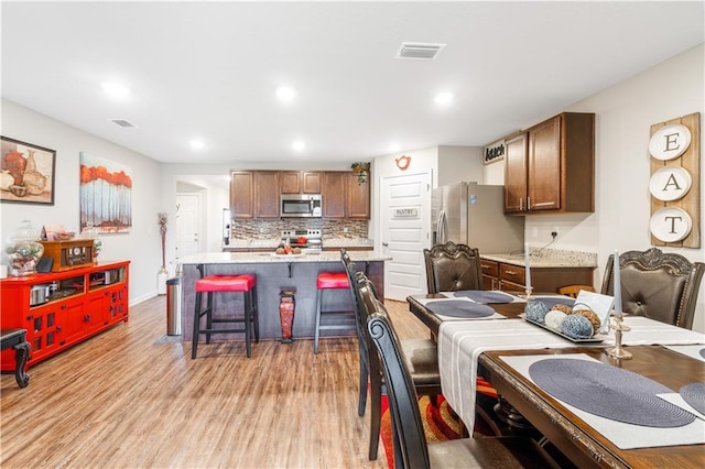 kitchen with appliances with stainless steel finishes, a kitchen island, light hardwood / wood-style floors, a kitchen bar, and decorative backsplash