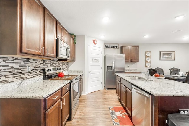 kitchen featuring sink, a center island with sink, light wood-type flooring, stainless steel appliances, and light stone countertops