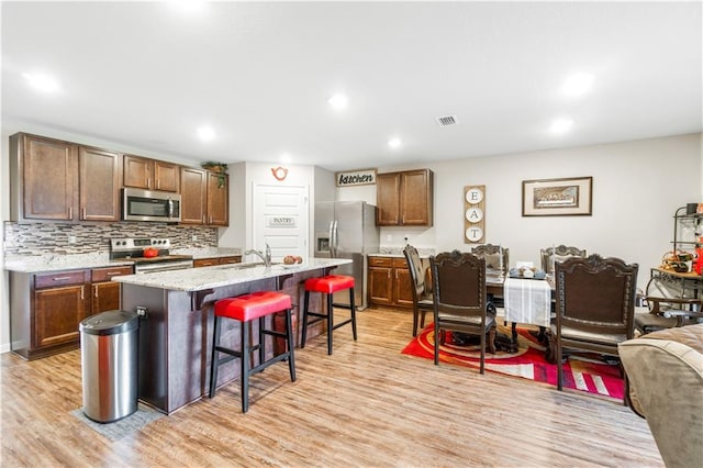 kitchen featuring a breakfast bar area, stainless steel appliances, tasteful backsplash, an island with sink, and light wood-type flooring