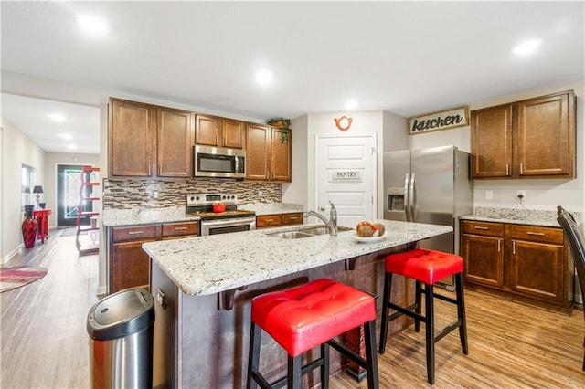 kitchen featuring light hardwood / wood-style floors, stainless steel appliances, an island with sink, and a kitchen bar