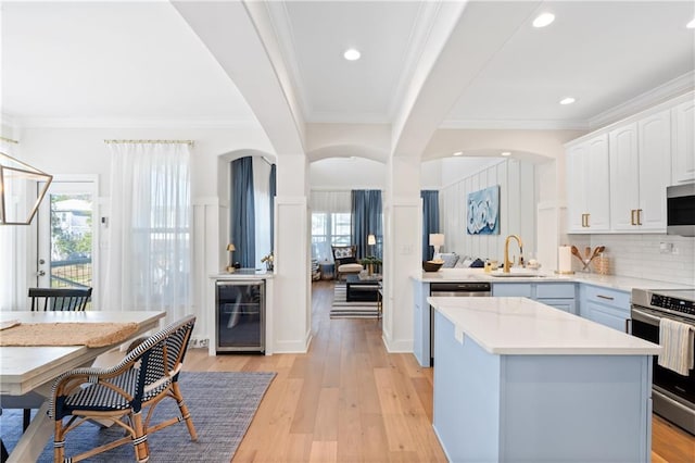 kitchen with wine cooler, a kitchen island, sink, white cabinetry, and appliances with stainless steel finishes