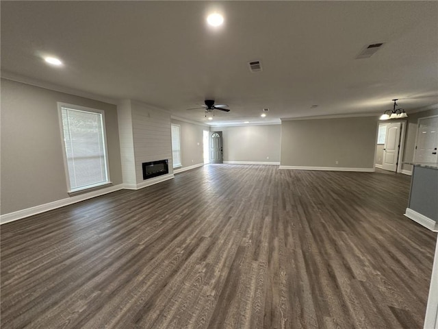 unfurnished living room with crown molding, a large fireplace, dark wood-type flooring, and ceiling fan with notable chandelier