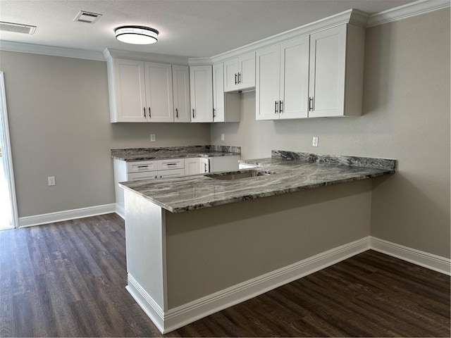 kitchen with dark wood-type flooring, stone countertops, white cabinetry, and ornamental molding