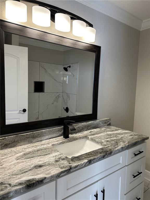 bathroom with vanity, ornamental molding, and tiled shower