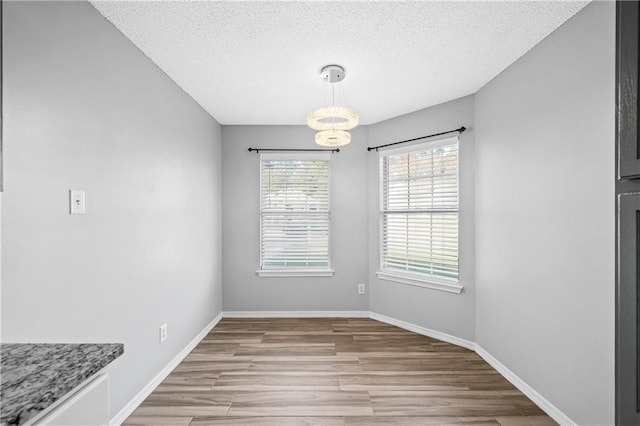 unfurnished dining area featuring wood finished floors, baseboards, a textured ceiling, and a chandelier