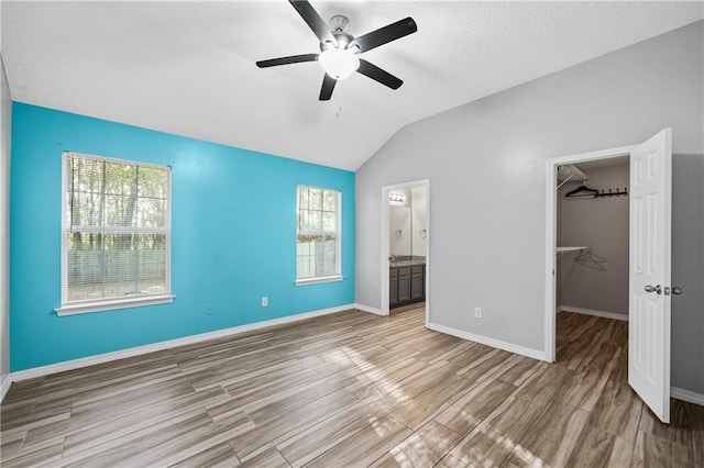 unfurnished bedroom with vaulted ceiling, a spacious closet, wood finished floors, and baseboards