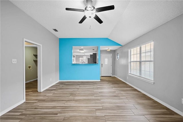 unfurnished living room with visible vents, baseboards, wood tiled floor, ceiling fan, and vaulted ceiling