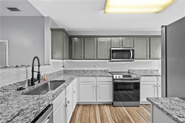 kitchen featuring a sink, backsplash, appliances with stainless steel finishes, and light wood-style flooring