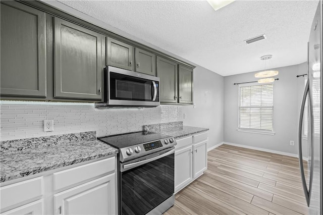 kitchen featuring tasteful backsplash, a textured ceiling, stainless steel appliances, light wood-style floors, and light stone countertops