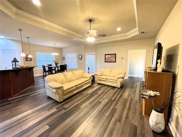 living room with ornamental molding, ceiling fan, dark wood-type flooring, and a raised ceiling