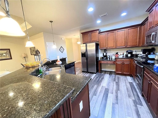 kitchen with dark stone counters, dark wood-type flooring, decorative light fixtures, sink, and appliances with stainless steel finishes