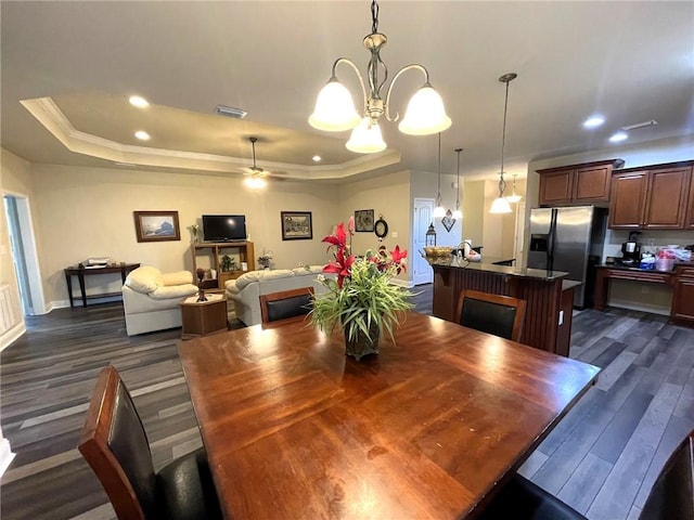 dining room with ceiling fan with notable chandelier, ornamental molding, a tray ceiling, and dark wood-type flooring