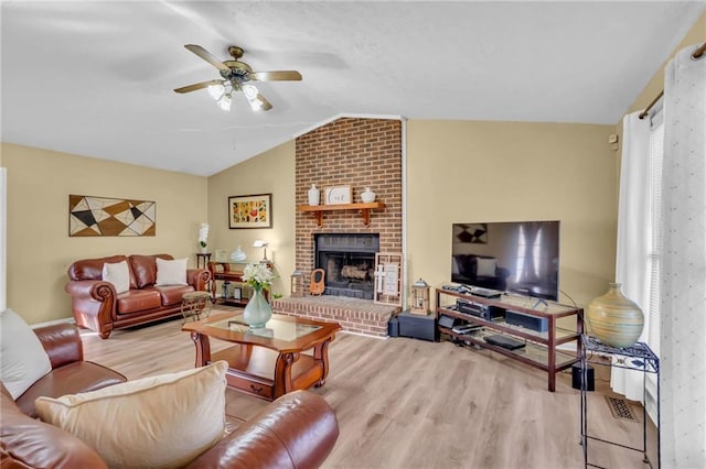 living room with a brick fireplace, ceiling fan, light wood-type flooring, and vaulted ceiling