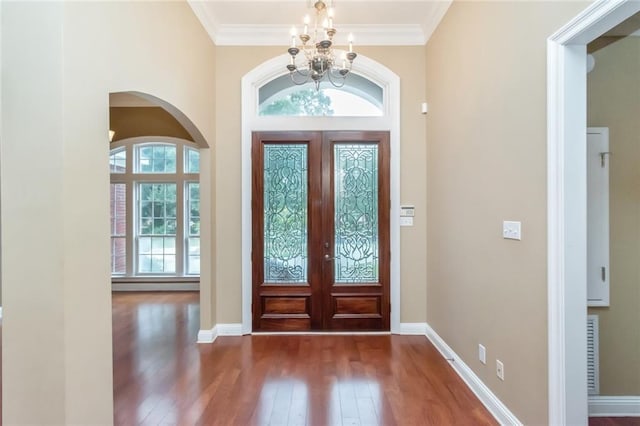 foyer entrance with dark wood-type flooring, ornamental molding, a chandelier, and french doors