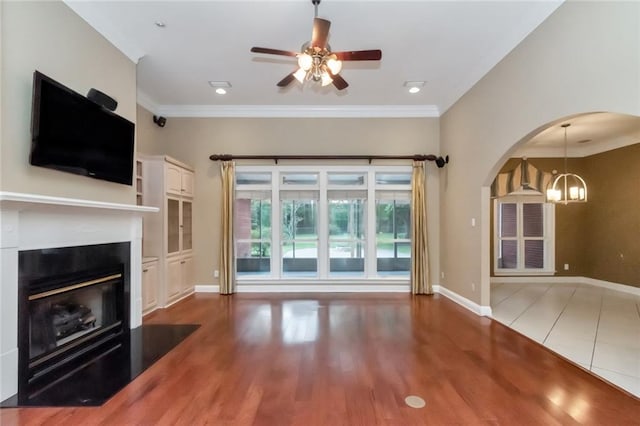 unfurnished living room featuring ceiling fan with notable chandelier, crown molding, and hardwood / wood-style floors