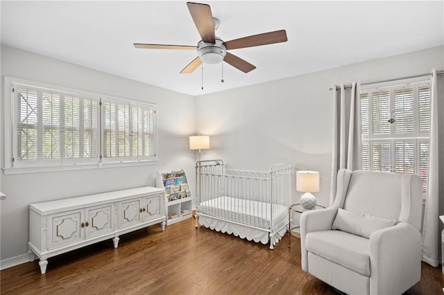 bedroom with ceiling fan, baseboards, a nursery area, and wood finished floors