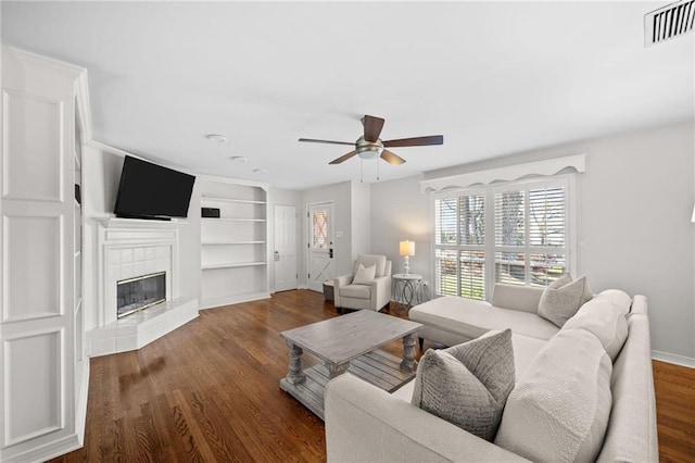living room with built in features, ceiling fan, a fireplace, visible vents, and wood finished floors