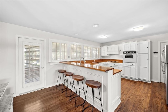 kitchen with stovetop, oven, a peninsula, and dark wood-style floors