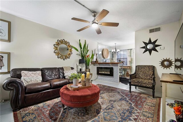 tiled living room with a textured ceiling, a fireplace, and ceiling fan with notable chandelier