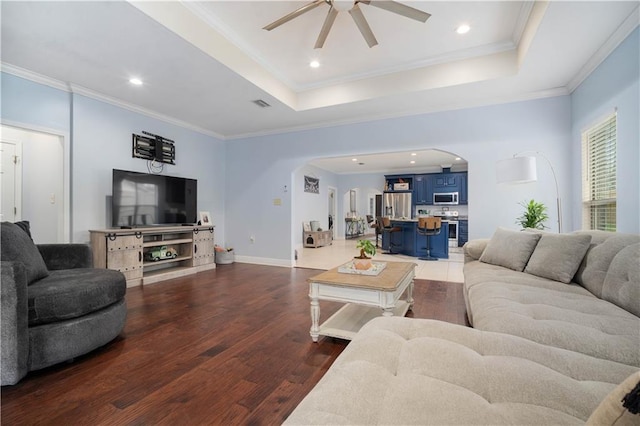 living area with visible vents, ornamental molding, dark wood finished floors, arched walkways, and a raised ceiling