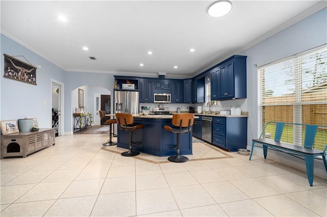 kitchen featuring a breakfast bar, blue cabinetry, appliances with stainless steel finishes, crown molding, and light tile patterned floors