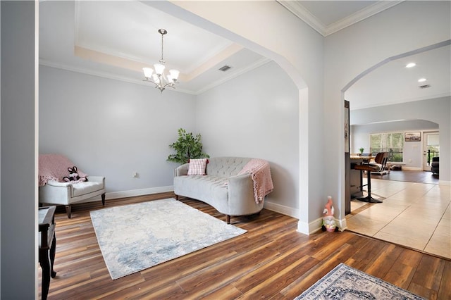 sitting room featuring a tray ceiling, arched walkways, wood finished floors, and crown molding