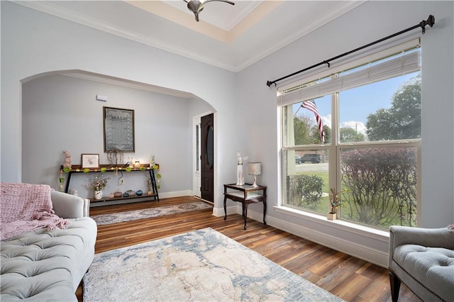 sitting room with crown molding, baseboards, wood finished floors, arched walkways, and a raised ceiling