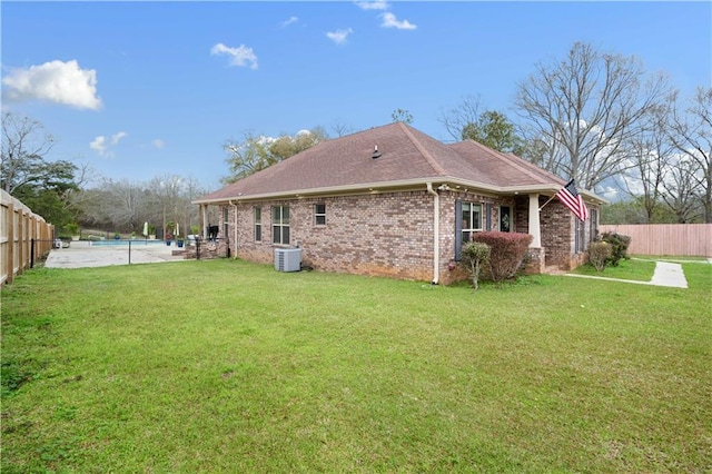 rear view of property with brick siding, a lawn, a fenced backyard, and central AC